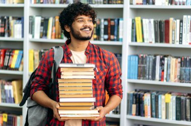 Zeki, pozitif Hintli ya da Arap milenyum çocuğu, üniversite öğrencisi, günlük giysiler içinde, kütüphanede duruyor, bir sürü kitabı elinde tutuyor, sınava hazırlanıyor, başka tarafa bakıyor, mutlu bir şekilde gülümsüyor.