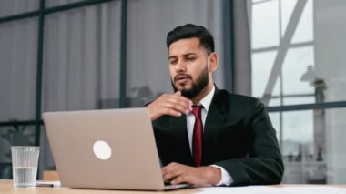 Yorgun Hintli ya da takım elbiseli Arap bir işadamı, işyerinde oturur, köprüsünü ovuşturur, uzun süre dizüstü bilgisayarla çalıştıktan sonra yorgunluk hisseder, çok çalışır, dinlenir, kahve molası verir.