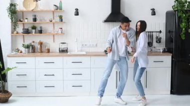 Genç, mutlu, aşık bir çift, yeni evliler, şık bir şekilde giyinmiş, evde en sevdikleri müzikle dans ediyorlar, iç mimari tarzlarıyla, gülümseyerek, birlikte vakit geçirmekten keyif alıyorlar.