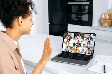 Sanal toplantı, iş arkadaşlarının beyin fırtınası, online sohbet. Afrika kökenli Amerikalı genç bir kadın araya girenleri selamlıyor, çok ırklı iş grubuyla görüntülü konuşma yapıyor, projeyi tartışıyor.