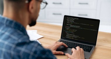 IT technology. Panoramic photo of a programmer with laptop. View over the shoulder of a guy, an IT specialist to a laptop screen, male programmer prescribes codes for an application, develops software