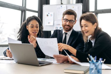 Bir projede iş ortakları birlikte çalışıyor. Çok ırklı meslektaşlar birlikte strateji üzerine beyin fırtınası yapıyorlar, modern ofiste oturup, belgeler üzerinde çalışıyorlar, dizüstü bilgisayar kullanıyorlar, tartışıyorlar, gülümsüyorlar.