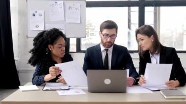 Bir projede iş ortakları birlikte çalışıyor. Çok ırklı meslektaşlar birlikte strateji üzerine beyin fırtınası yapıyorlar, modern ofiste oturup, belgeler üzerinde çalışıyorlar, dizüstü bilgisayar kullanıyorlar, tartışıyorlar, gülümsüyorlar.