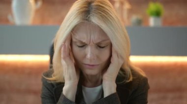 Close-up of a tired exhausted middle aged caucasian business lady, experiencing fatigue from work, overwork, suffering from headache, migraine, massages her temples, closed her eyes, needs rest