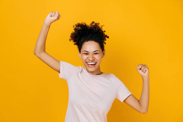 Good news, success and happiness concept. Excited happy curly-haired african american woman, dancing, gesturing with fists, receives profit, glad to win lottery, standing on isolated orange background