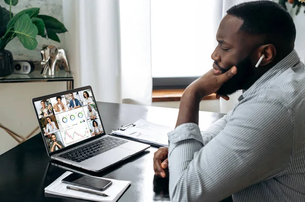 Online business meeting, briefing. African american successful entrepreneur, ceo, sitting at a desk, having a financial brainstorm with colleagues on a video conference, analyzing a financial strategy
