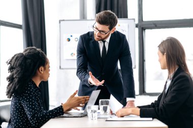Elegant Caucasian intelligent male boss, holding group brainstorm with female colleagues, discussing ideas for a new business project, analyzes report and profit, explain info