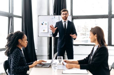 Elegant Caucasian intelligent male boss, holding group brainstorm with female colleagues, discussing ideas for a new business project, makes a business plan presentation to his female partners