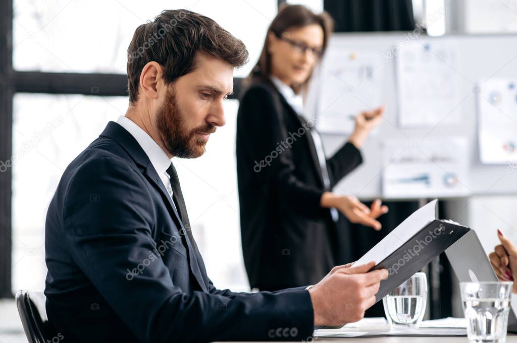 Busy focused intelligent caucasian business man in a formal suit, sit at workplace in a modern office, looks out the documents, financial reports, planning strategy, analyzing risks