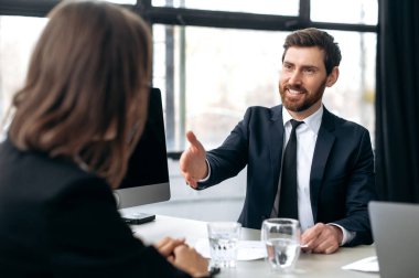 Caucasian influential attractive successful businessman, development boss, ceo company, shakes hands with female colleague in modern office, smile at each other. Shaking hands, making deal, agreements