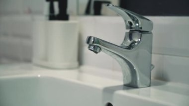 Static video of a faucet in a bathroom with dripping water. Faucet malfunction, drops of clean water dripping into the white washbasin
