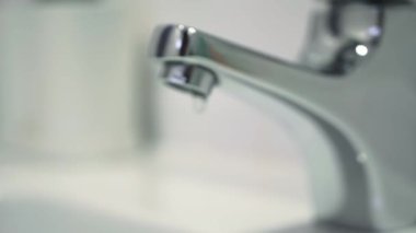 Water leak concept. Close up of water drops.Video of a faucet in a bathroom with dripping water. Faucet malfunction, drops of clean water dripping into the white washbasin