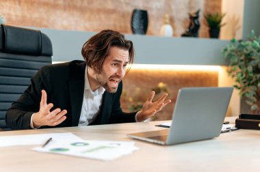 Irritated angry caucasian business man, stock trader, product manager, working in a modern office, yelling to the laptop, frustrated by the disruption of an important deal, financial losses, upset