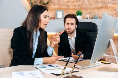 Cooperation concept. Two successful caucasian employees, business partners, sit at a table in the office, look at computer screen, study the companys financial prospects and risks with concentration