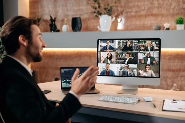 Successful caucasian male stock broker sits in his modern office, talking on a video call with colleagues, working out a crypto strategy, discussing risks. Video conference with business partners