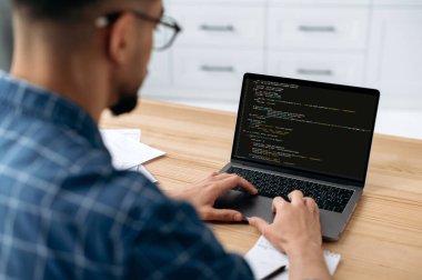 Photo of a programmer with laptop. View over the shoulder of a guy, an IT specialist to a laptop screen, male programmer prescribes codes for an application, develops software. IT technology