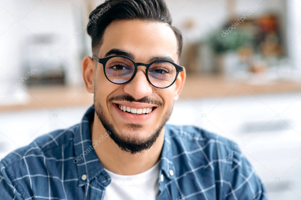 Close-up photo of a handsome attractive mixed race young man with glasses, freelancer or student, in casual shirt, with perfect white teeth, looking at the camera with toothy happy smile