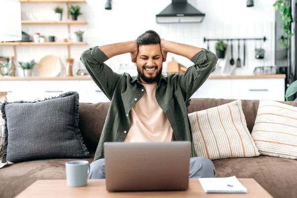 Shocked confused indian or arabian young man, freelancer, designer, looking surprised at laptop screen, stressed from the failure of a deal or project, read unexpected news, in desperation, annoyed