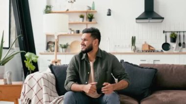 Sad Arabian or Indian man, dressed in casual wear, trying to get up off the couch, experiencing acute pain in the back, lower back, has chronic joint problems. Problems with the back, spine, sciatica