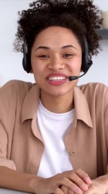 Vertical video of a pretty African American stylish girl with headset, mentor or student, conducts an online meeting with colleagues or students, holds a speech about company ideas and plans, smile