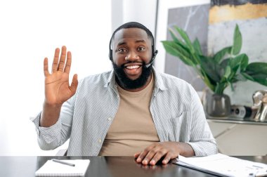 Friendly positive african american man with headset, business leader or coach, conducts business meeting with colleague, discuss ideas and promotion, talks about strategy, records online lesson, smile