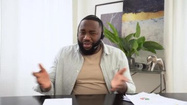 Confident african american man with headphones, business leader, company employee, having online business conversation, listens to the interlocutor, conducts consultation, takes notes, smiles