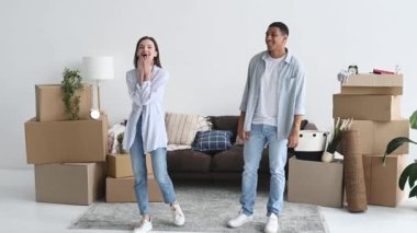 Happy multiracial young couple in love looks their new home, look around the interior with excited, rejoice at their new home, dancing, hugging, smile. Moving to a new apartment