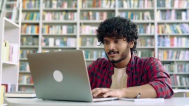 Amazed happy excited stylish mixed race guy, student, sitting in university library with laptop, rejoices in success, win, good mark on the exam, gesturing hands, smiling, emotional face expression