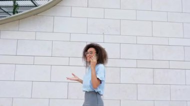 Mutlu Afro-Amerikan kıvırcık saçlı, mavi iş gömleği giyen, gözlüklü, dışarı çıkan, bir toplantıya giden, akıllı telefonla konuşan, yüzünü çeviren, el kol hareketi yapan, gülen,