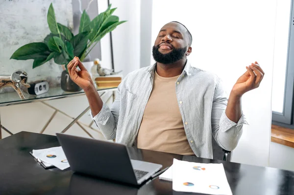 Relaxed calm peaceful African American stylish man, freelancer, designer, company ceo, taking a break, resting from online work or study in a laptop, meditating with closed eyes, relaxing, smiling