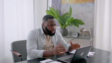 Irritated angry stressed african american man, sit at desk in the office, using laptop for online work, annoyed with bad result of his project, failed the deal, experiences negative emotions, stress