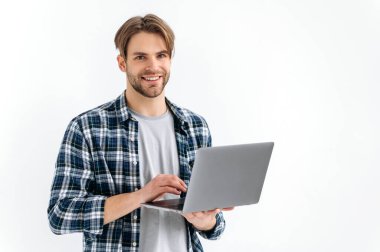 Positive handsome confident caucasian stylish young man, freelancer, student, programmer, standing on a white isolated background, holds an open laptop, looking to the camera, smiling friendly