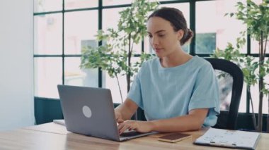 Joyful amazed happy brazilian or hispanic young business woman, sitting at a desk with a laptop in modern office, rejoicing in success, big profit, celebrate deal, gesturing with fists, smiling