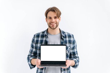 Model konsepti. Gündelik giyinen yakışıklı beyaz adam, serbest çalışan, öğrenci, elinde boş maket alanı olan açık bir dizüstü bilgisayar, beyaz izole edilmiş arka planda duruyor, kameraya bakıyor, gülümsüyor.