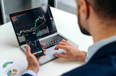 Akıllı telefon tutan erkek ellerinin yakın çekimi. Borsa kripto döviz piyasası için cep telefonu uygulamasını kullanan tüccar yatırımcı analisti, grafik ticareti veri endeksi yatırım büyüme grafiğini analiz eden, strateji planlayan