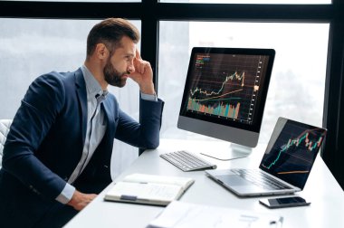 Odaklanmış başarılı beyaz erkek yatırımcı, borsacı, çalışma masasına oturur, bilgisayara bakar, riskleri ve umutları analiz eder, kripto para biriminin yükselişi ya da düşüşü, planlama stratejisi