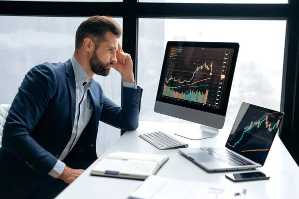 Odaklanmış başarılı beyaz erkek yatırımcı, borsacı, çalışma masasına oturur, bilgisayara bakar, riskleri ve umutları analiz eder, kripto para biriminin yükselişi ya da düşüşü, planlama stratejisi