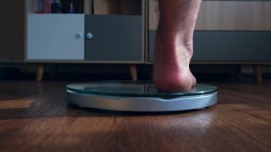 Erkek, oturma odasındaki terazide duran vücut ağırlığını ölçer. Yüksek kalite 4k görüntü