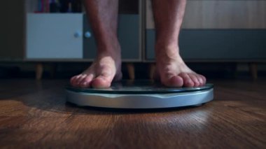 Erkek, oturma odasındaki terazide duran vücut ağırlığını ölçer. Yüksek kalite 4k görüntü