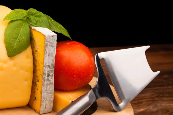 Various types of cheese and tomato on wooden table isolated on black — Stock Photo, Image