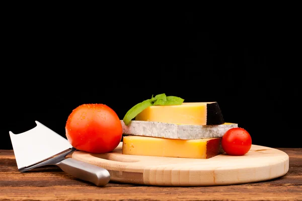 Various types of cheese and tomato on wooden table isolated on black — Stock Photo, Image