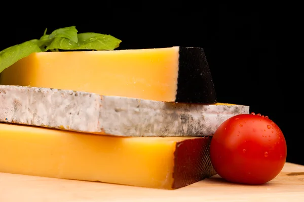 Various types of cheese and tomato on wooden table isolated on black — Stock Photo, Image