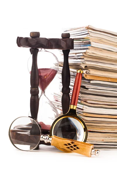 Pile of newspapers magnifying glass and hourglass — Stock Photo, Image