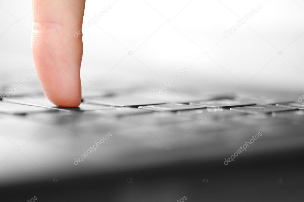 Human finger pressing button on laptop computer