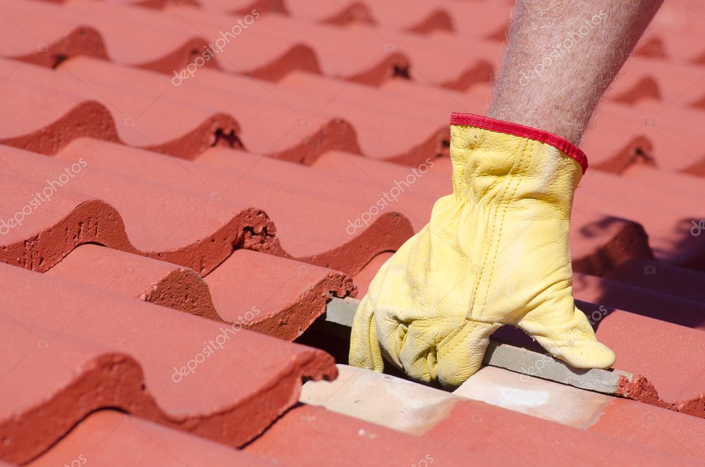 Roof repair, worker with white gloves replacing gray tiles or shingles on  house with blue sky