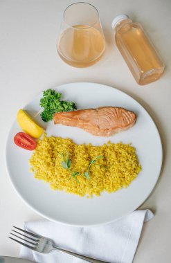 Düzgün beslenme, günlük diyet, kilo kaybı. Yeşiller, domatesler, limonlu somon bifteği ve bir tabakta kuskus garnitürü. Üst görünüm