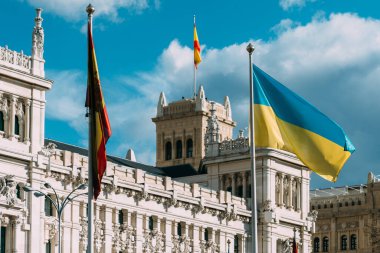 The flag of Spain and Ukraine flutter in the wind in front of Cibeles in Madrid, Spain. European Union and Spanish solidarity concept as Russia invaded Ukraine in February 2022 clipart