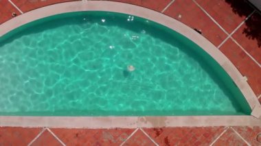 Havadan aşağıya doğru yaklaşan kadın şapkası güneş ışığında havuzda yüzerken görülüyor.