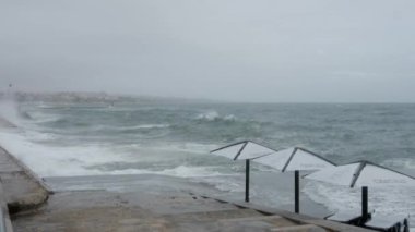 Sonbahar fırtınaları sırasında Portekiz, Cascais 'deki sahil şeridine boş güneş pansiyonlarıyla su sıçratan dalgalardan püskürtün.