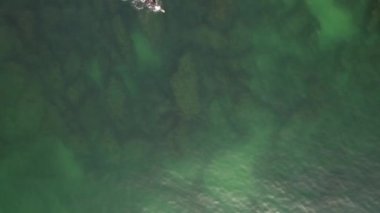 Türkuaz suda serbest yüzen, tanımlanamayan bir erkeğin yukarıdan aşağıya hava görüntüsü.